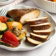Sliced piece of grilled sesame chicken on a plate with grilled vegetables.