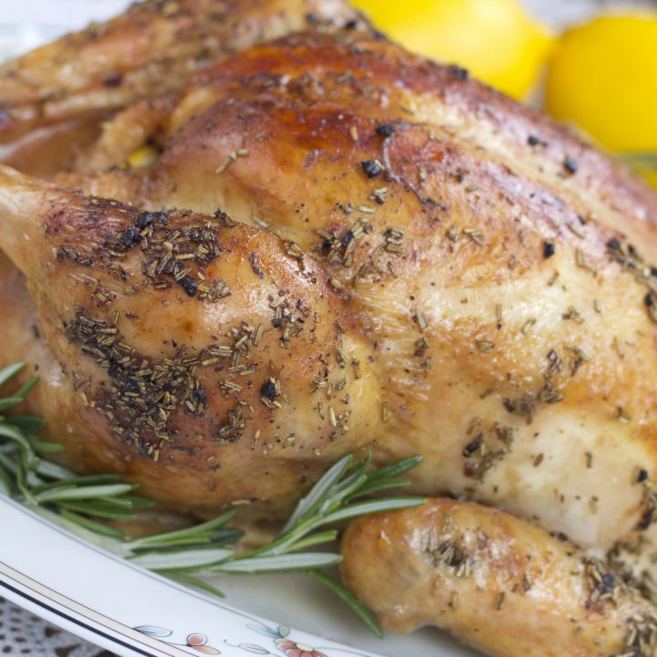 Whole roasted chicken on a platter with lemons and herbs