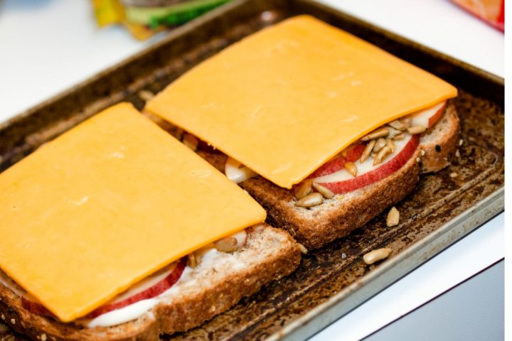 Open-faced Apple Cheddar Melt Sandwich with bread, mayo, apple slices, sunflower seeds, and cheddar and text Add Salt & Serve